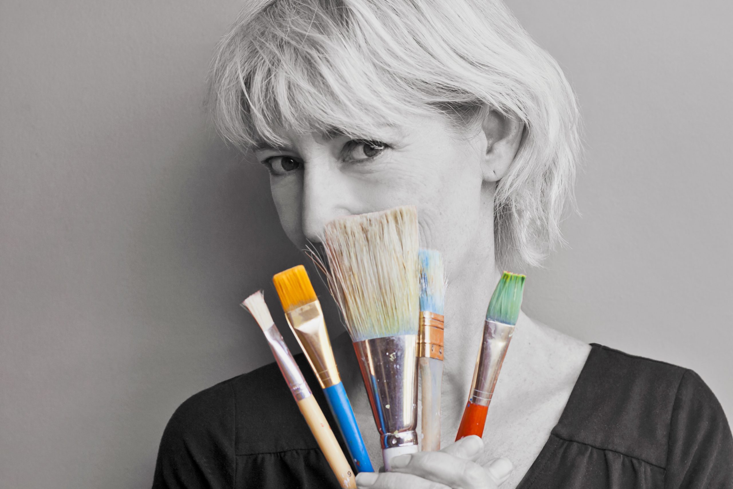 Lady with short hair holding up paint brushes