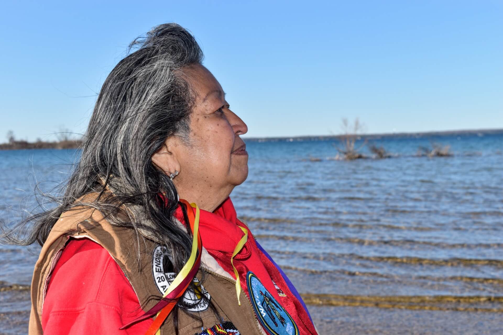 A woman in red in front of the water looking away