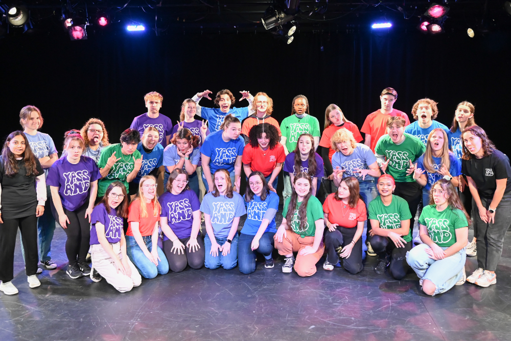 A large group of college students wearing multi-colored t-shirts and smiling