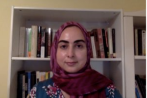 A young person smiles while sitting in front of a bookshelf.