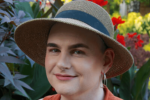 Ava Winter smiling at the camera. They are wearing a wide brimmed gray hat.