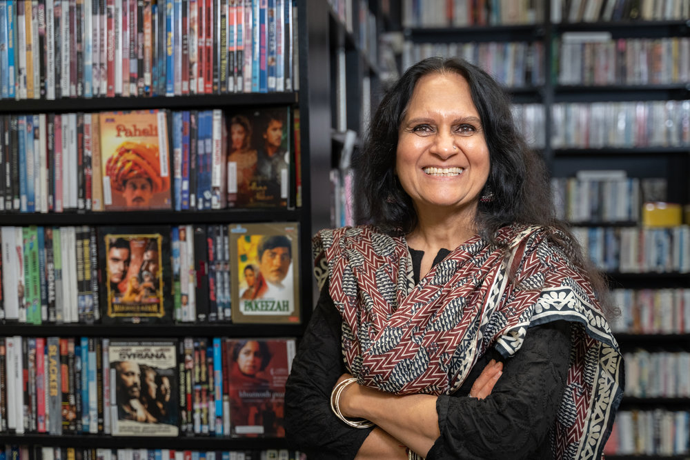 Woman with brown skin tone standing in front of book cases smiling at camera