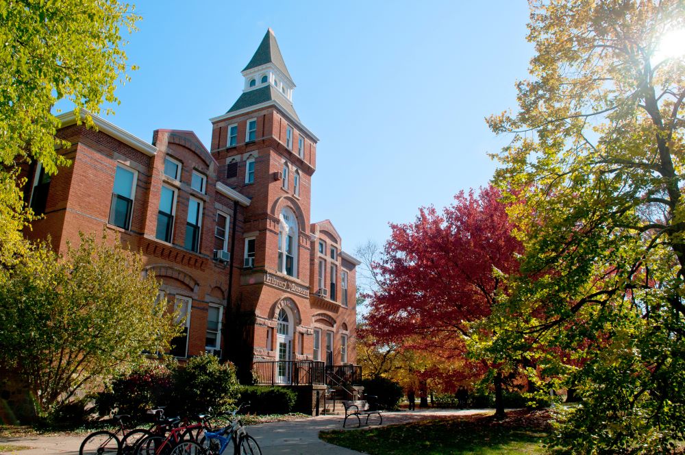 Historic brick building on Michigan State University's campus with blue skies and trees of green, red, and yellow autumn leaves