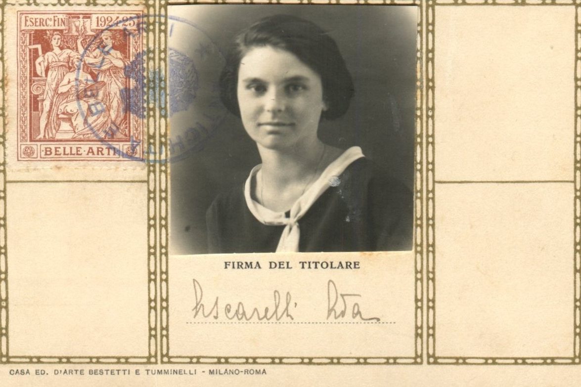 A vintage black-and-white identification card or postcard featuring a portrait of a young woman with dark hair tucked behind her ears, wearing a dark garment with a white collar. To the left is a red postage-style stamp with classical figures; below the portrait, the Italian text "FIRMA DEL TITOLARE" appears above a cursive signature.